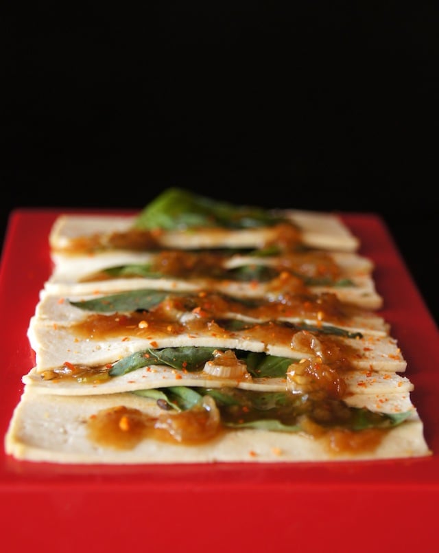 Tofu Vegan Sashimi with absil leaves lined up on a small red platter.