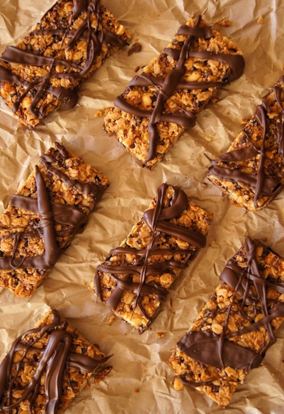 Several granola bars drizzled with chocolate on parchment paper.