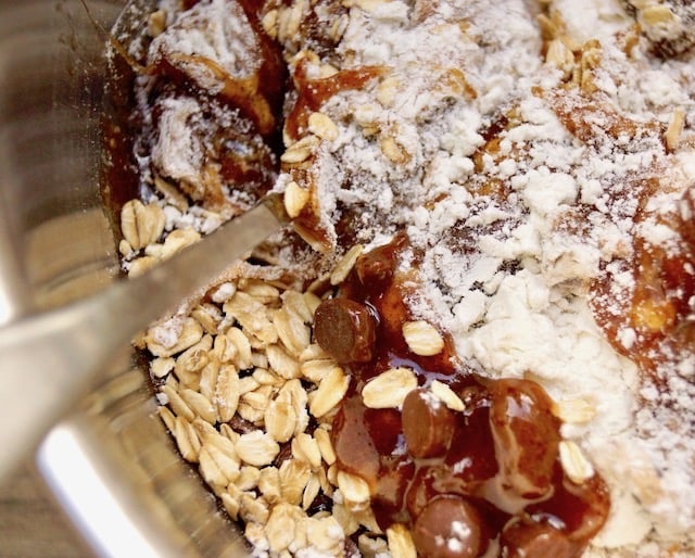 un-mixed ingredients for oatmeal raisin chocolate chip cookies in mixing bowl with spoon