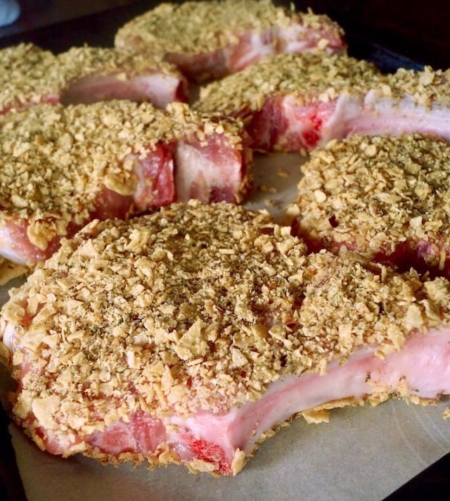 Raw pork chops with coating of tortilla chips and spices.