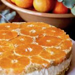 Upside down tangerine cheesecake with a big bowl of tangerines behind it.