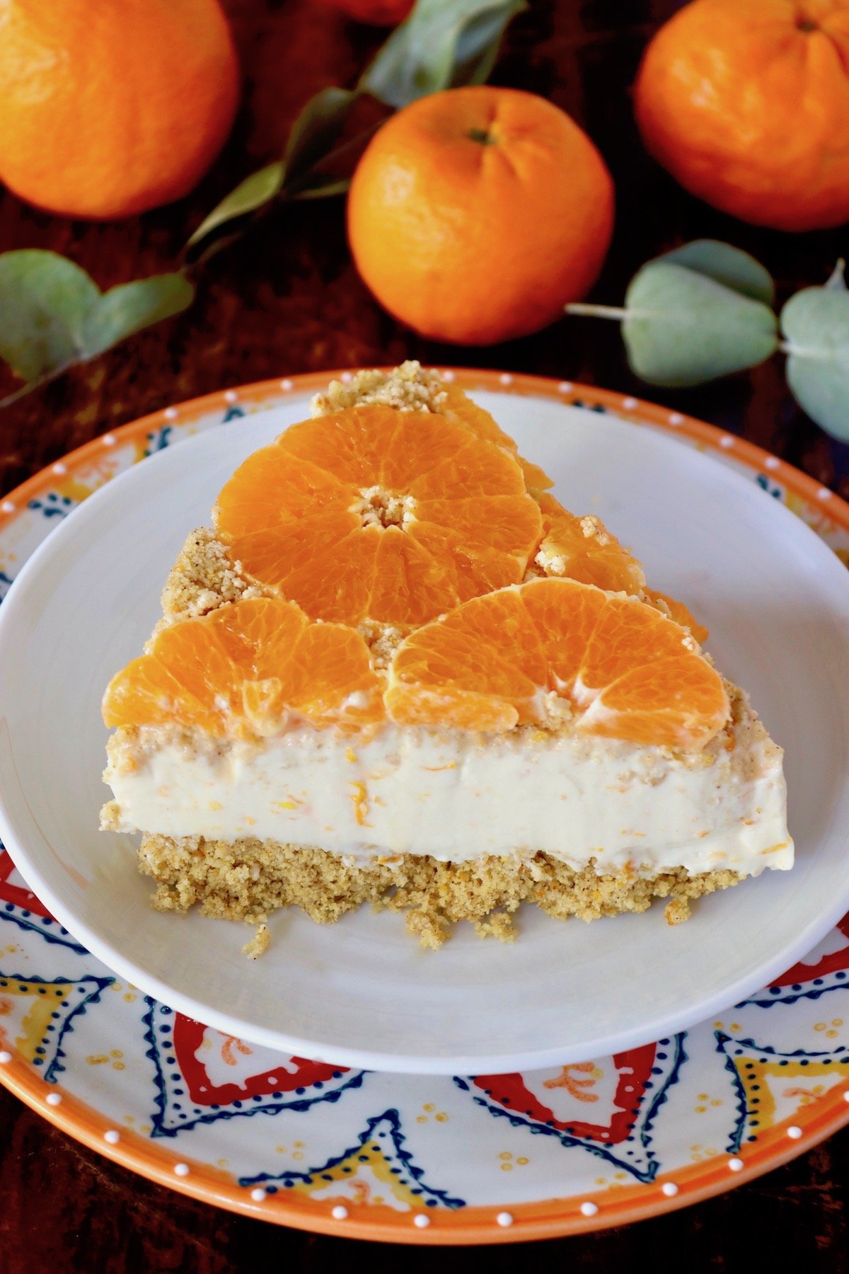 One slice of tangerine cheesecake on a white plate with an orange-rimmed plate beneath it.