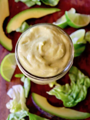 Top view of Mason jar full with creamy avocado dressing surrounded by slices of lime and avocado.
