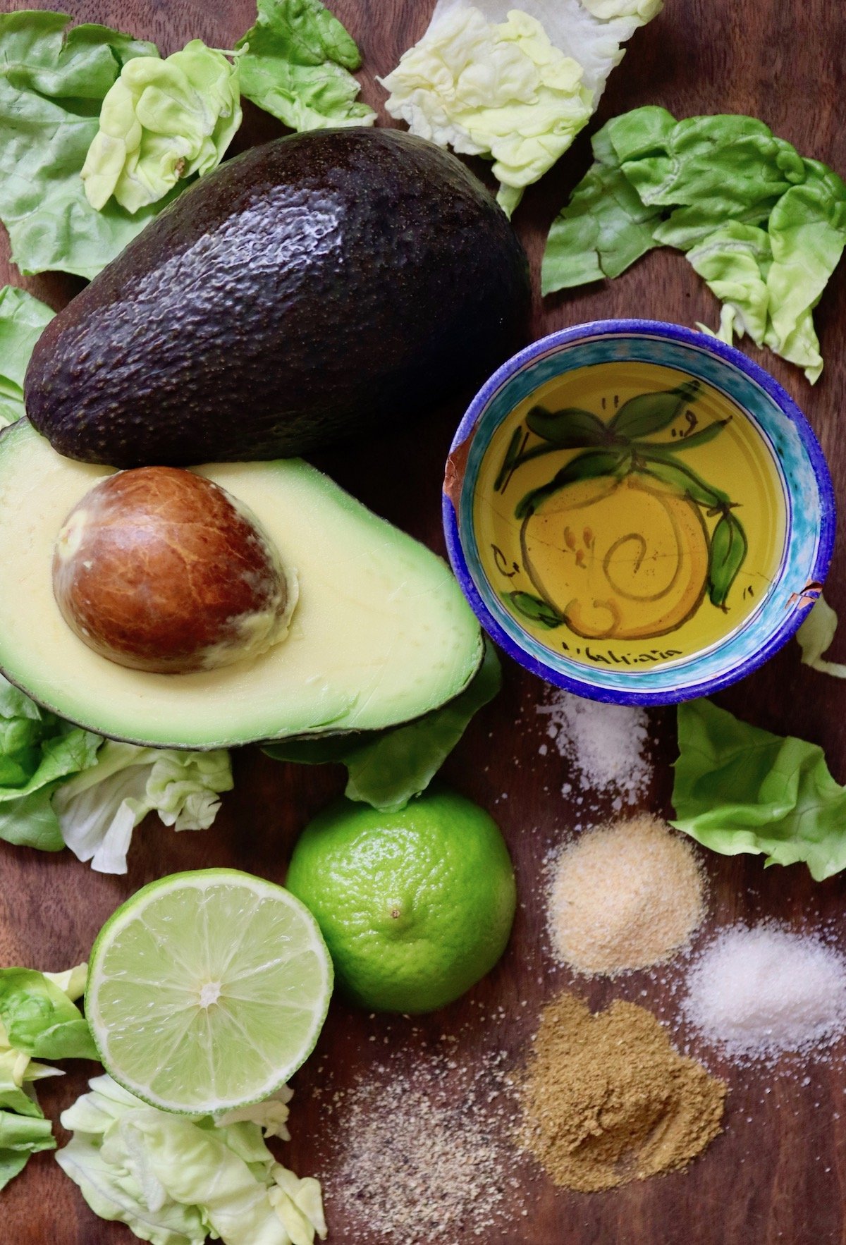 Ingredients for avocado dressing including avocado. limes, olive oil, salt, sugar, cumin and garlic powder.