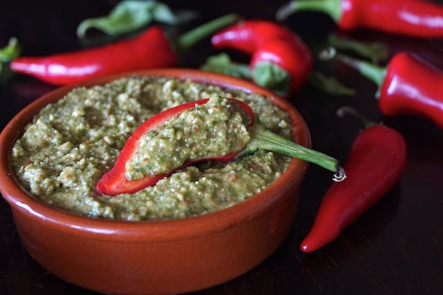Fresno Pepper Pesto in a terra cotta bowl with red peppers around it.
