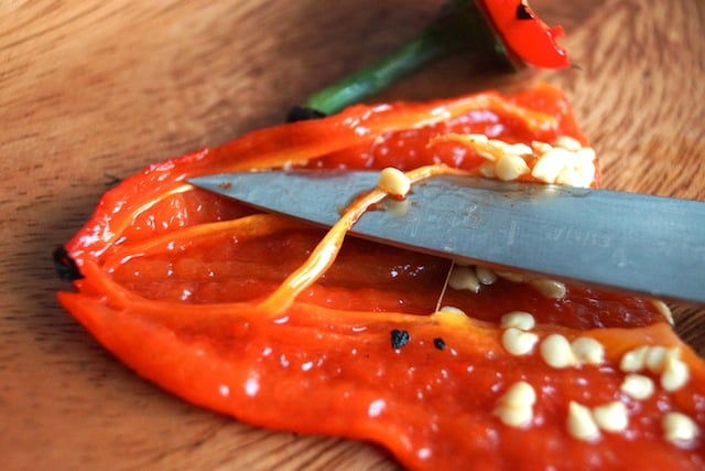 The inside of a roasted red pepper with a paring knife and seeds showing.