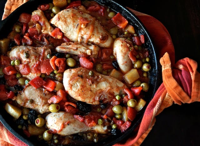 top view of Cuban Chicken Stew Recipe with Alcaparrado in cast iron skillet with cloth orange napkin wrapped abound handle
