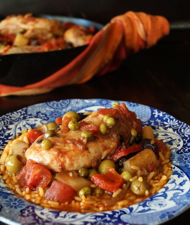 Cuban Chicken Stew Recipe with Alcaparrado in a pretty blue bowl with pan behind it