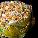 Close up of stuffed artichoke on black background.