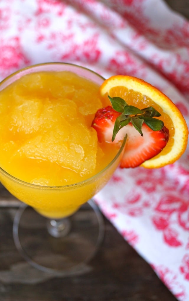 Mothers Day Mimosa Granita Cocktail in a wine glass with a slice of orange and strawberry on the rim.