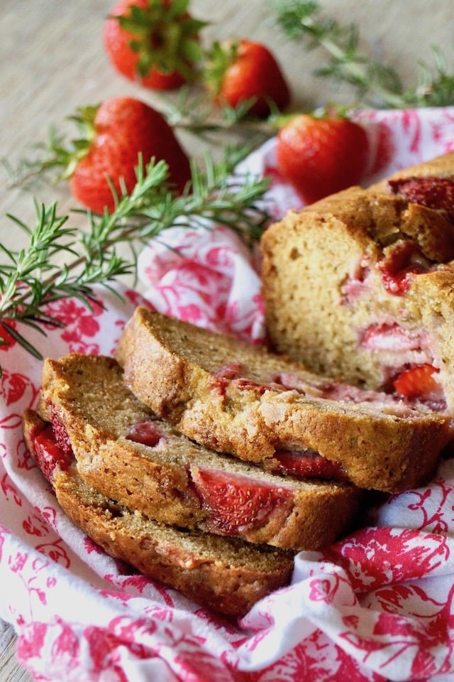 Sliced Strawbery-Rosemary Cake on a white and pink cloth with fresh rosemary sprigs.