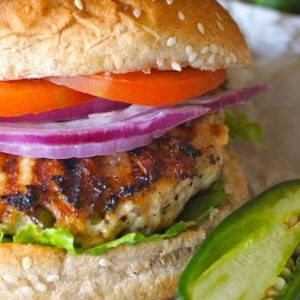 Jalapeno Pepper Jack Turkey Burger with red onion and tomato on parchment paper with one jalapeno sliced in half.