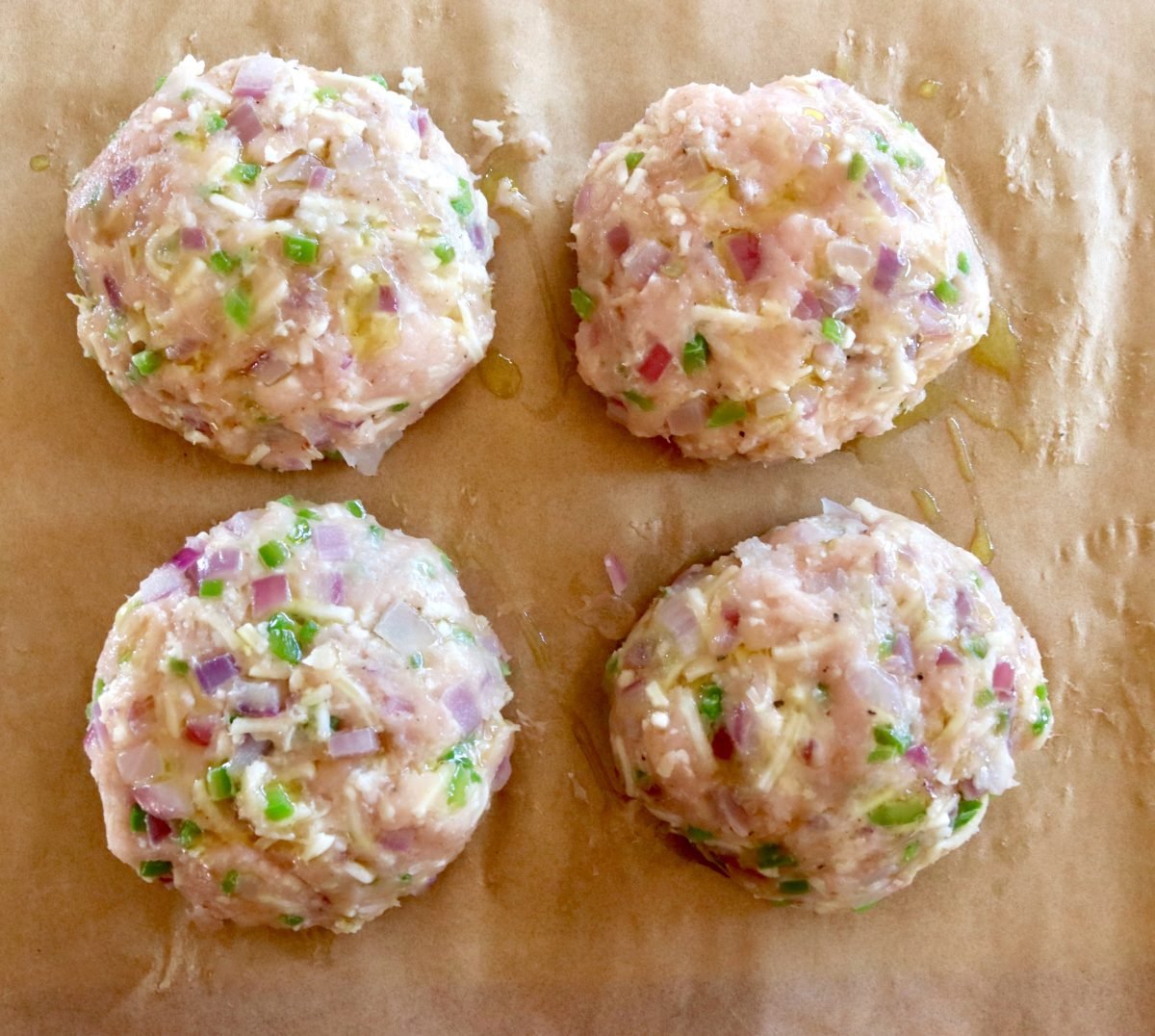 Four raw, shaped Turkey Burgers on parchment paper.