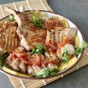 Pineapple Pork chops and sliced with pineapple slices and cilantro, on a white plate.