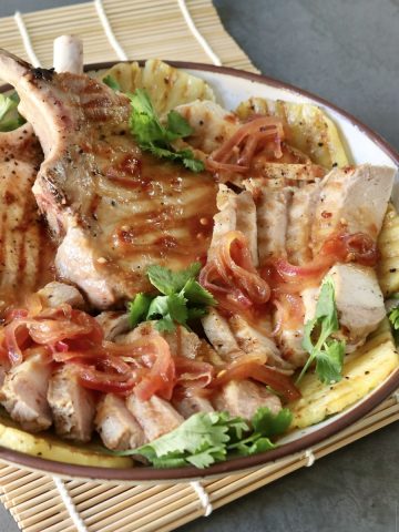 Pineapple Pork chops and sliced with pineapple slices and cilantro, on a white plate.