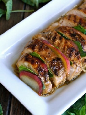sliced, grilled chicken with peaches and basil on white plate