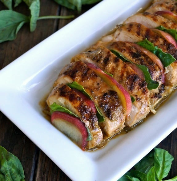 Peach Grilled Chicken with Basil on a narrow white plate surrounded iwth fresh bsil leaves.