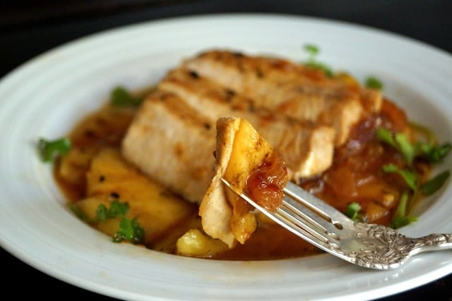 Sweet and Spicy Grilled Pineapple Pork Chop, sliced on a white plate with one bite on a fork.