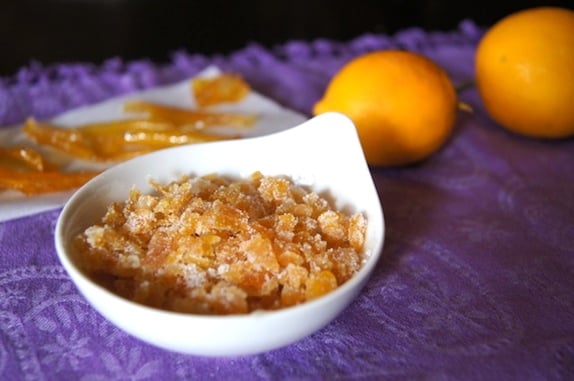 Candied Citrus Peels in a small white bowl on a purple cloth with 2 orange Meyer lemons in the background.
