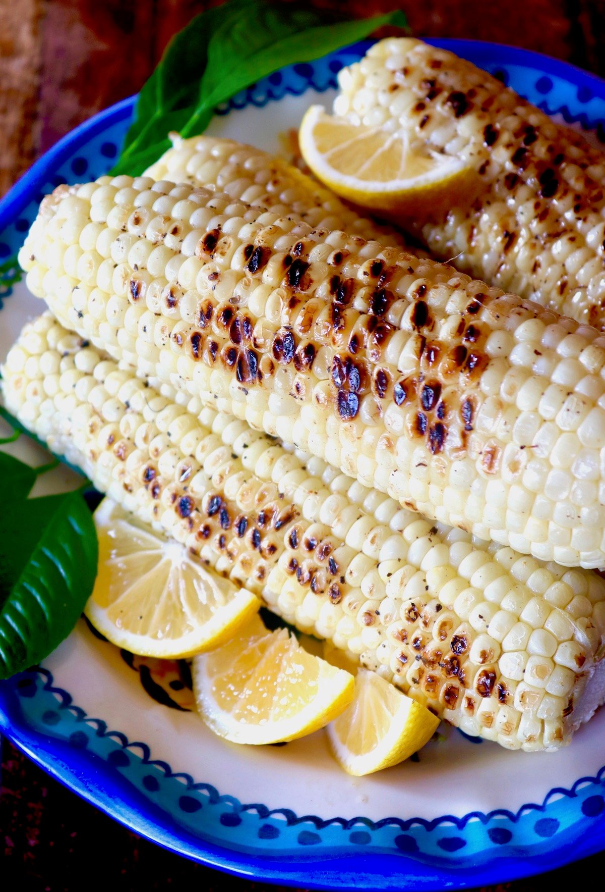 Pile of lemon-pepper grilled corn on a blue-rimmed plate with slices of lemon.