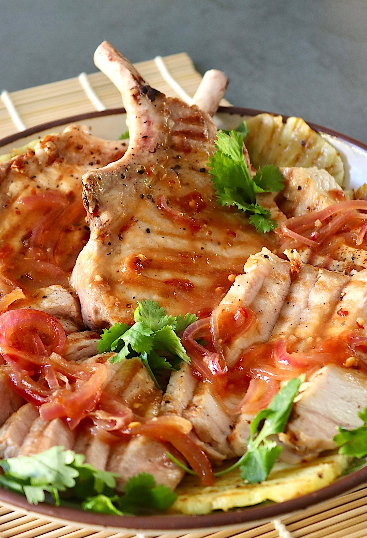 Pineapple Pork chops and with pineapple slices and cilantro, on a white plate.