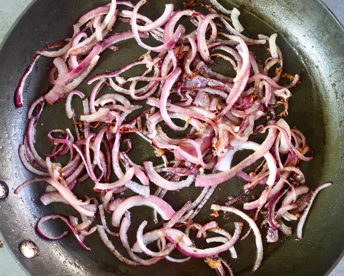 Sauteed red onion slices in a skillet.