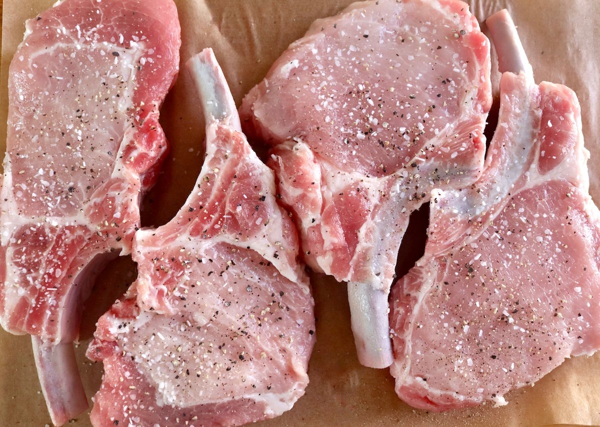 Raw pork chops sprinkled with salt and pepper.