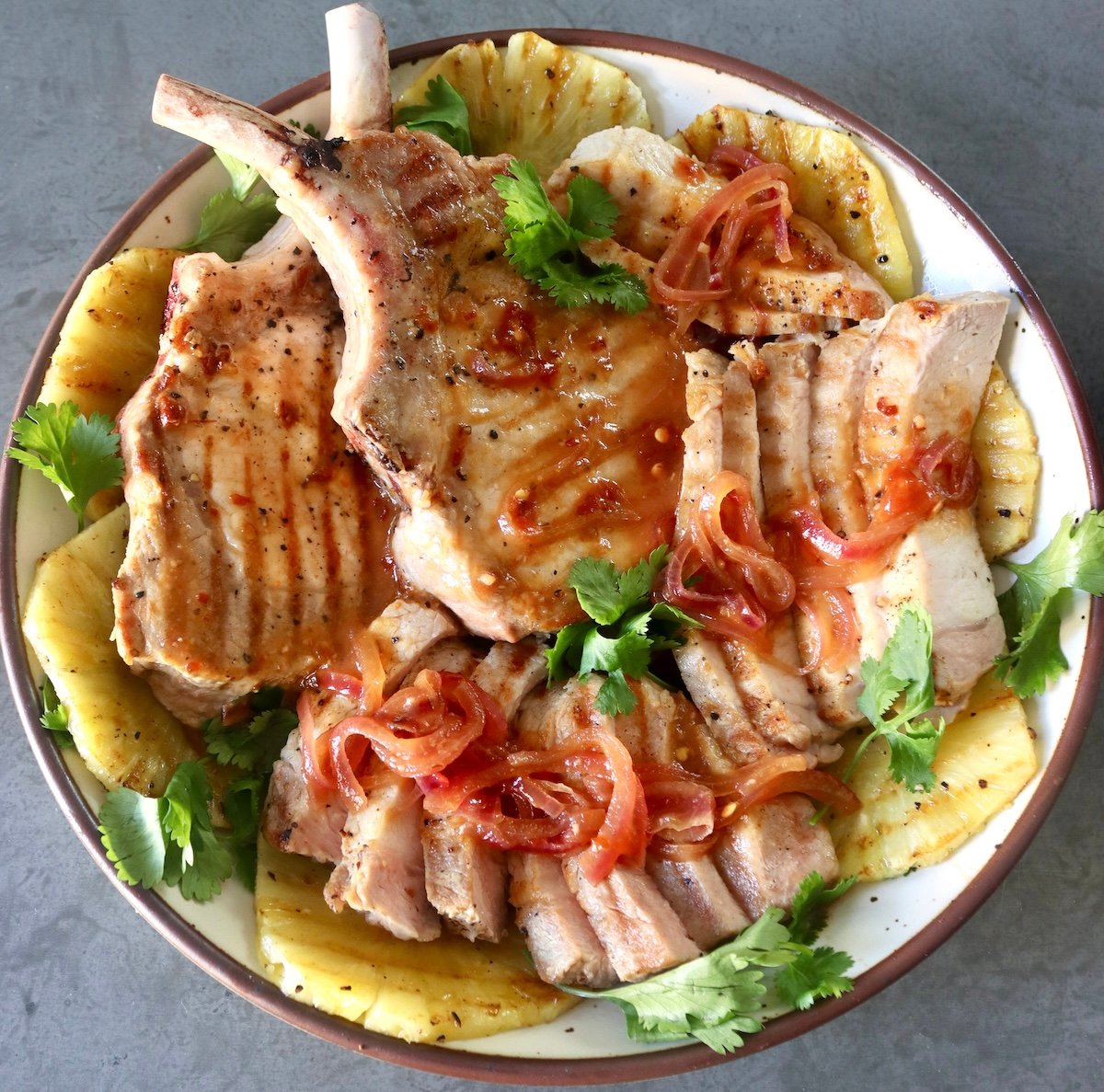 Top view of Pineapple Pork chops and sliced with pineapple slices and cilantro, on a white plate.