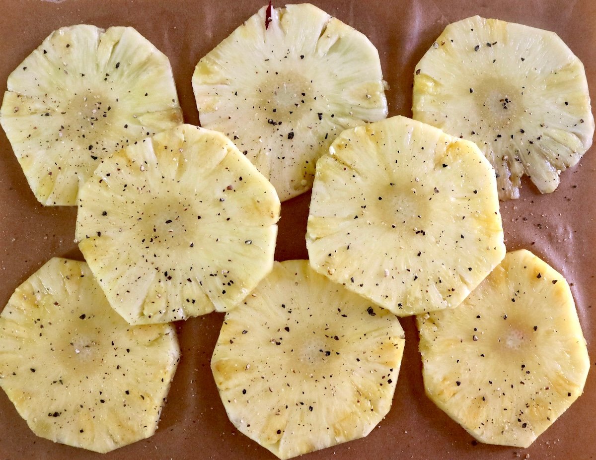 Several round pineapple slices sprinkled with salt and pepper.