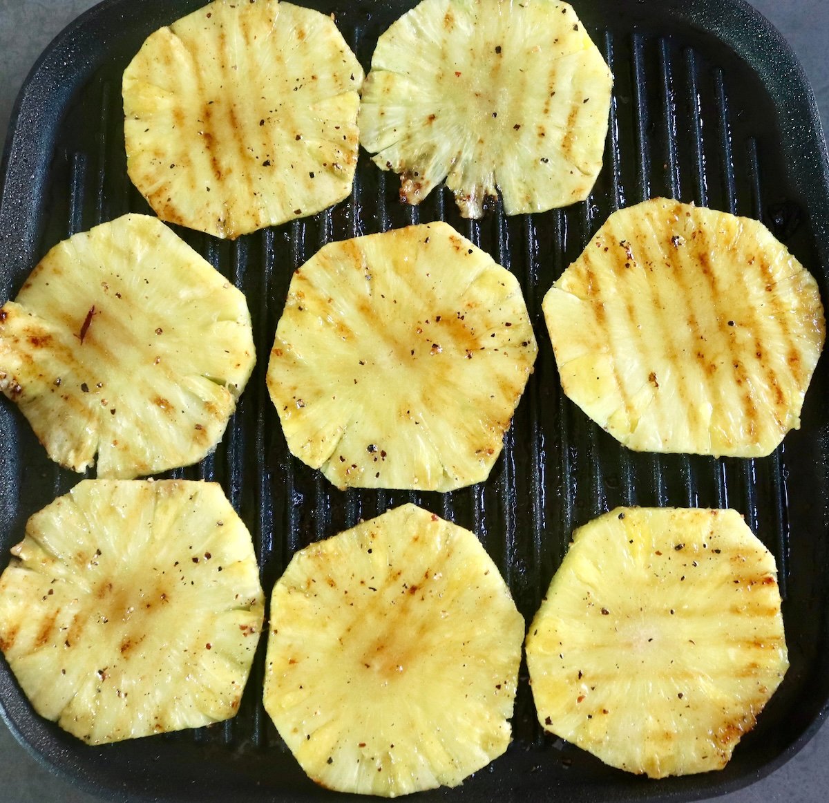 Grilled pineapple rounds on a grill, with grill marks.