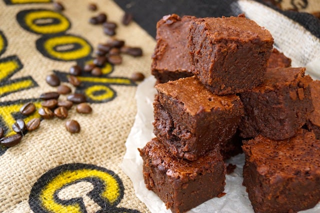 Several stacked Kona Coffee Kahlua Brownies surrounded by coffee beans on burlap bag.