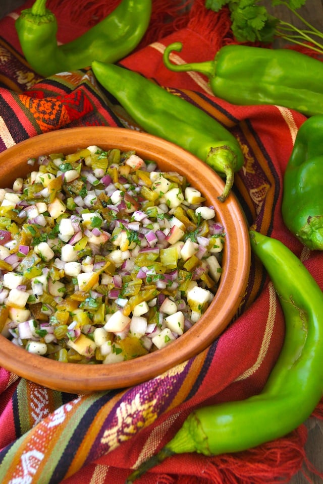 Roasted Hatch Chile Peach Salsa in a large teracotta bowl, surrounded by whole raw Hatch chiles.