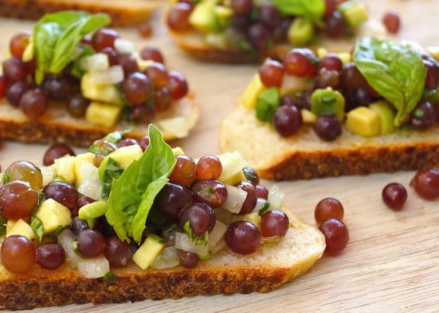 a few Bruschetta with Champagne Grapes on wood board with basil