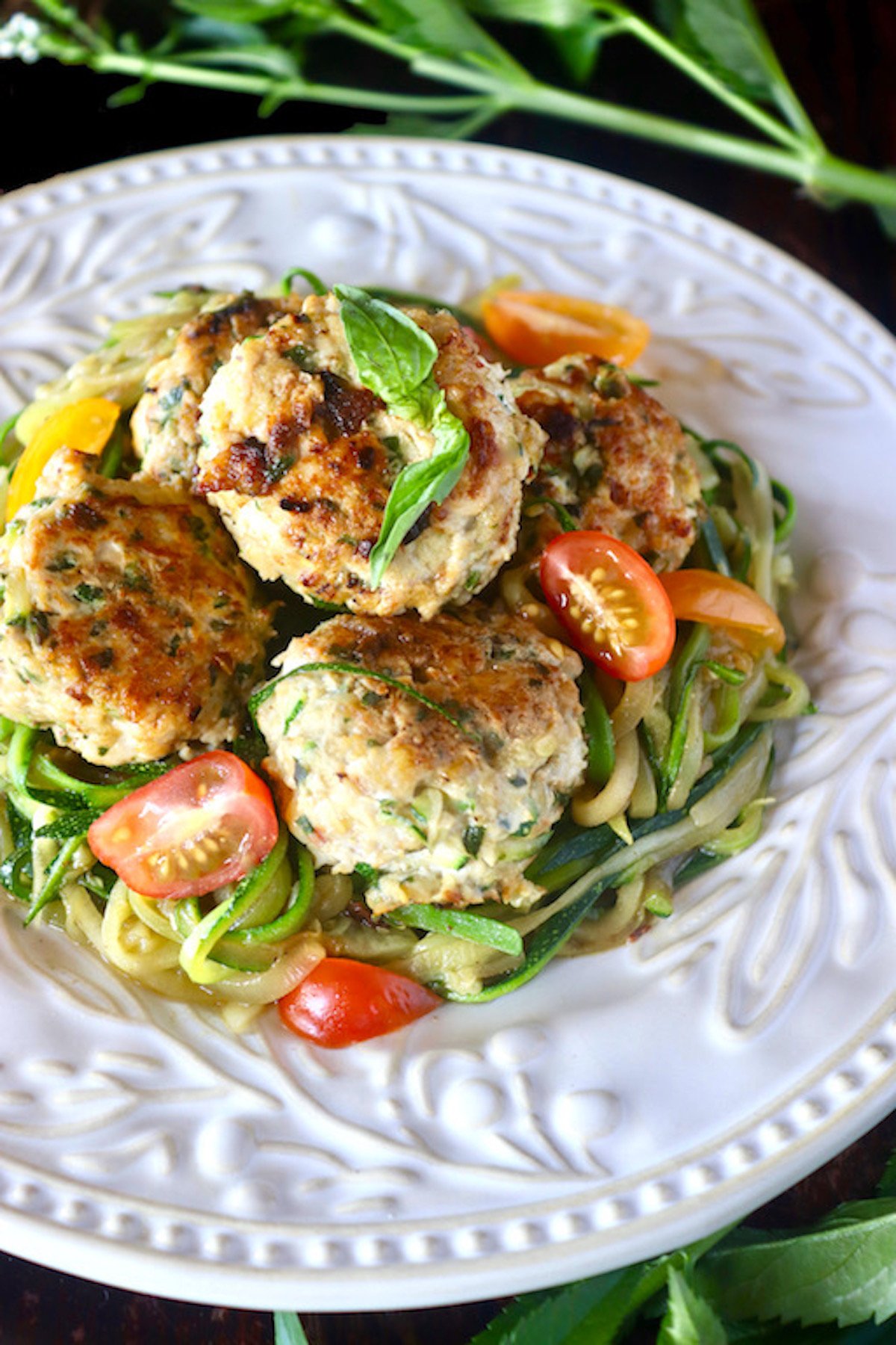 White plate with pattern on the edges full with large turkey zucchini meatballs and zoodles.