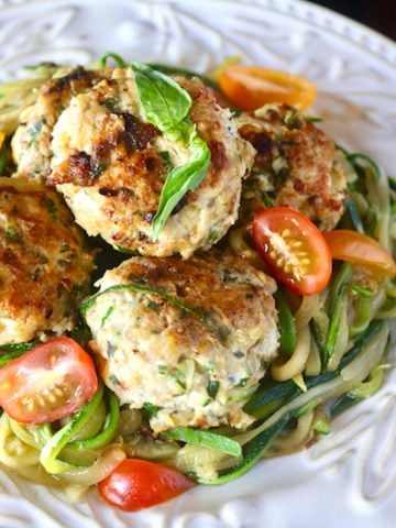 White plate with pattern on the edges full with large turkey zucchini meatballs and zoodles.