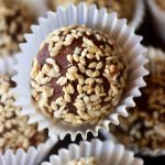 Close up of a sesame seed coated chocolate truffle in white paper cup.