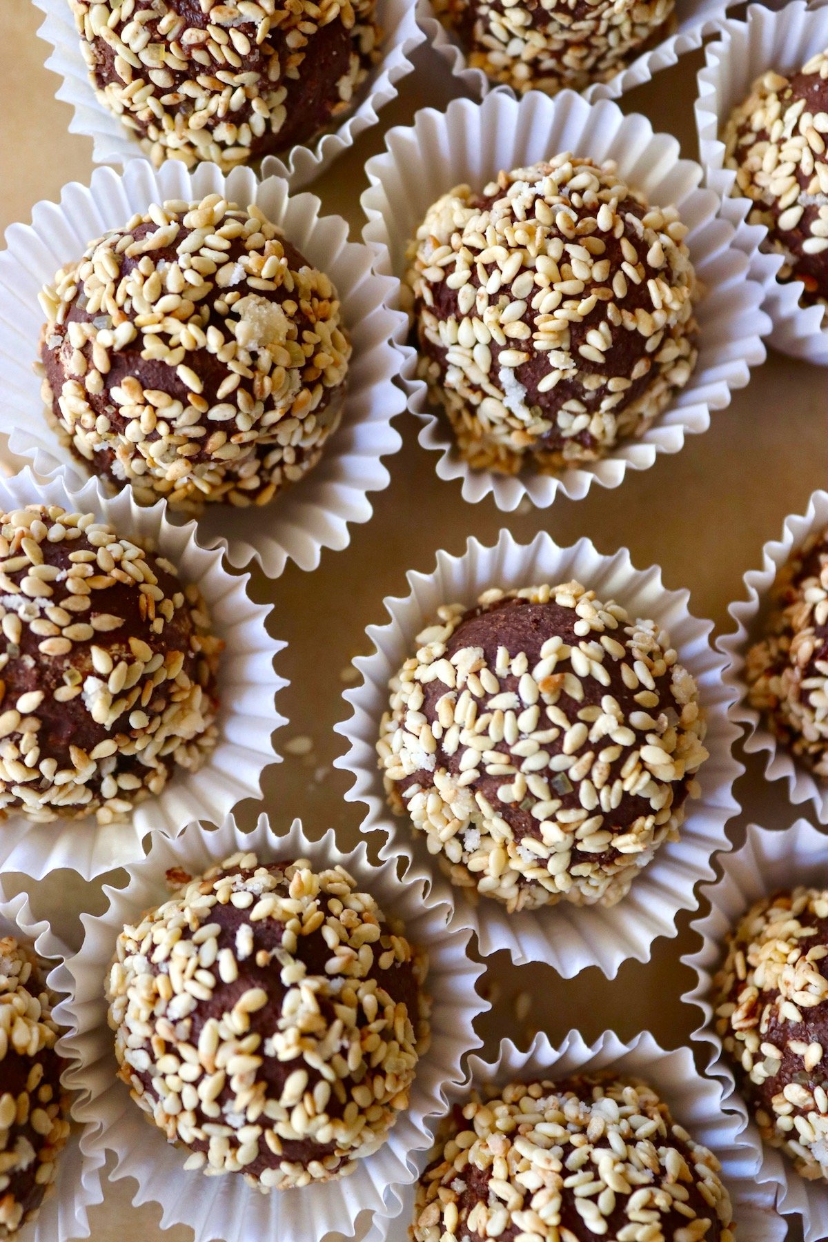 Several sesame seed coated chocolate truffles in white paper cups.