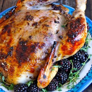 Roasted Chicken with Blackberry Butter on a blue platter with fresh blackberries.