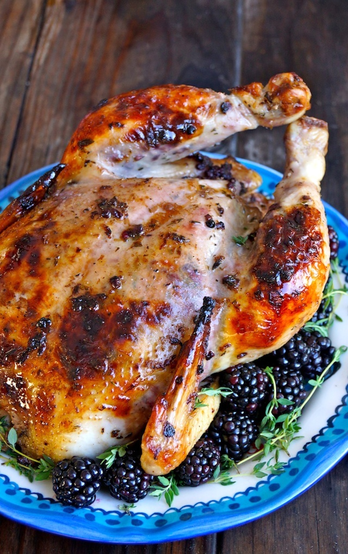 Whole Roasted Chicken with Blackberry Butter and fresh blackberries and fresh thyme, on a blue-rimmed ceramic platter.