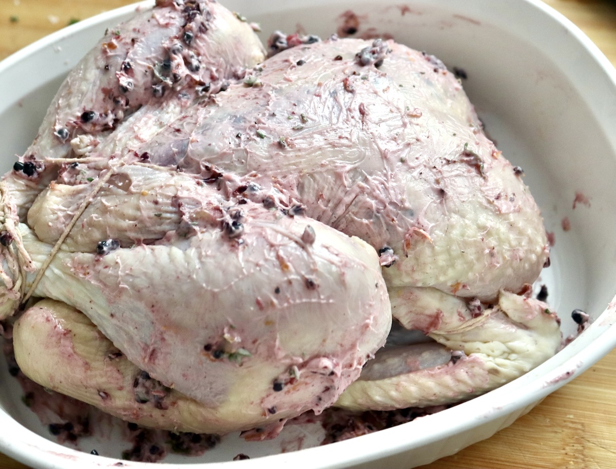 Blackberry-Chicken-Recipe-with-Blackberry-Butter) Whole trussed chicken rubbed with blackberry butter in a white roasting pan.