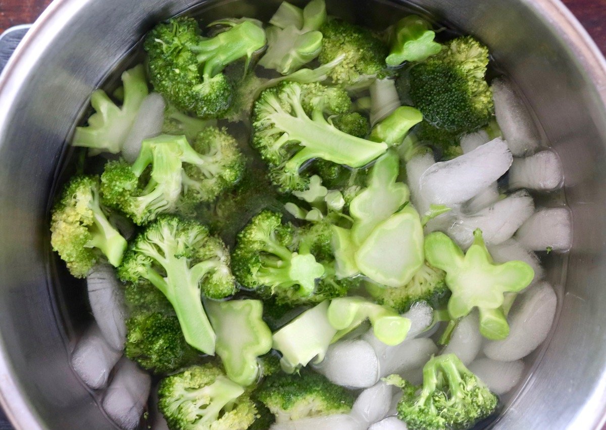 Cooked bright green broccoli in a bowl of ice water.