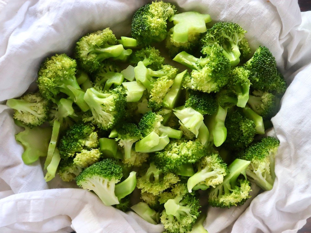 Pile of bright green broccoli in a white kitchen towel.