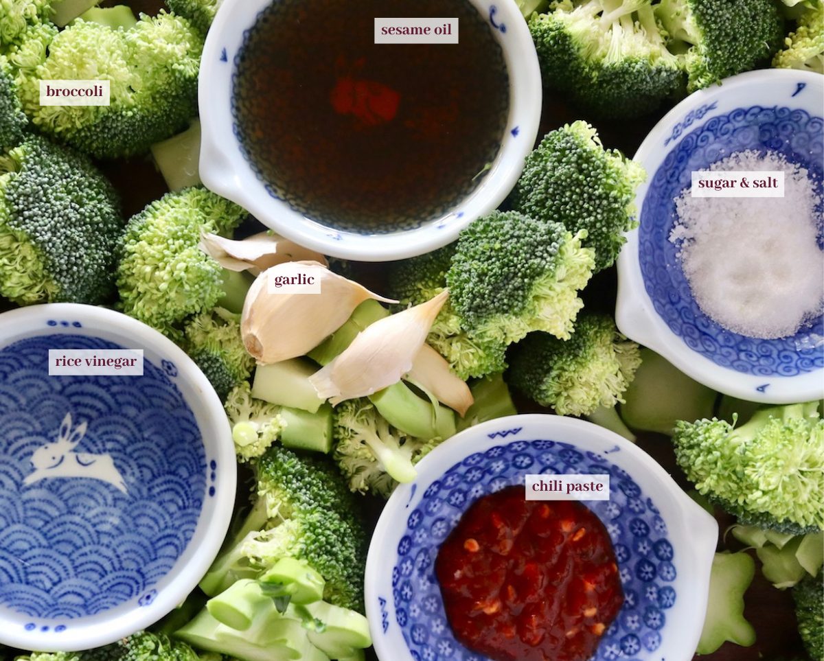 Broccoli florets spread out on cutting board with tiny blue bowls between them with Asian sauces and sugar.