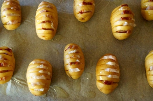 Baby Dutch Yellow Potatoes with many slits in them, with bacon in each one, on parchment