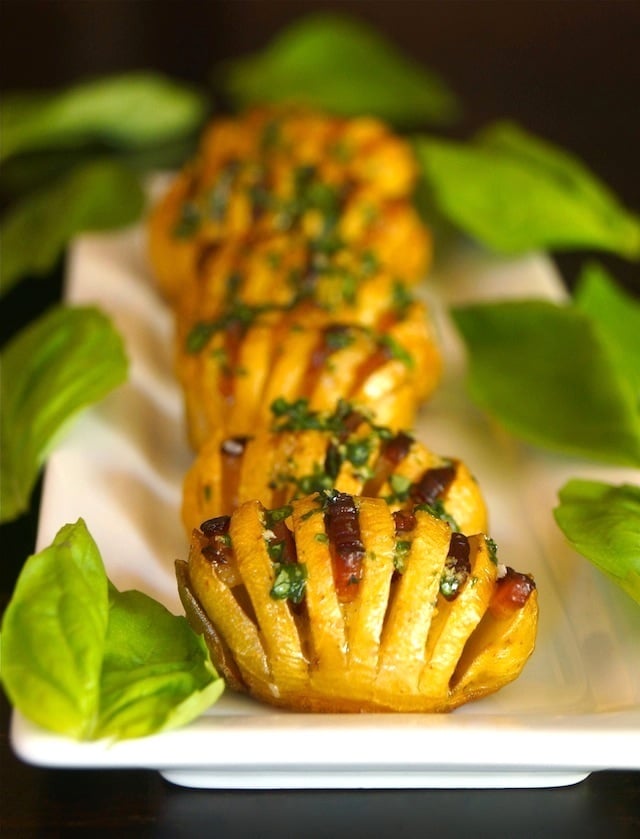 Bacon Basil Hasselback Dutch Yellow Potatoes lined up on a white plate with fresh basil leaves