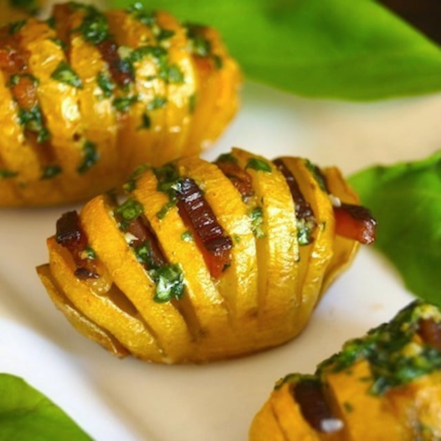 mimi hasselback potatoes with bacon on a white plate with basil