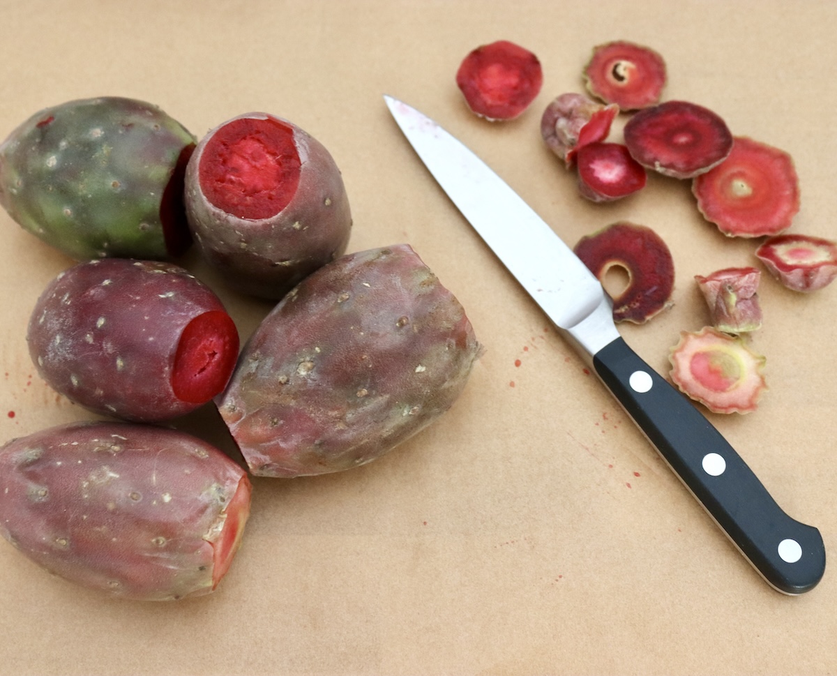Several prickly pears (cactus pears) with both ends cut off, on a cutting board with a paring knife.