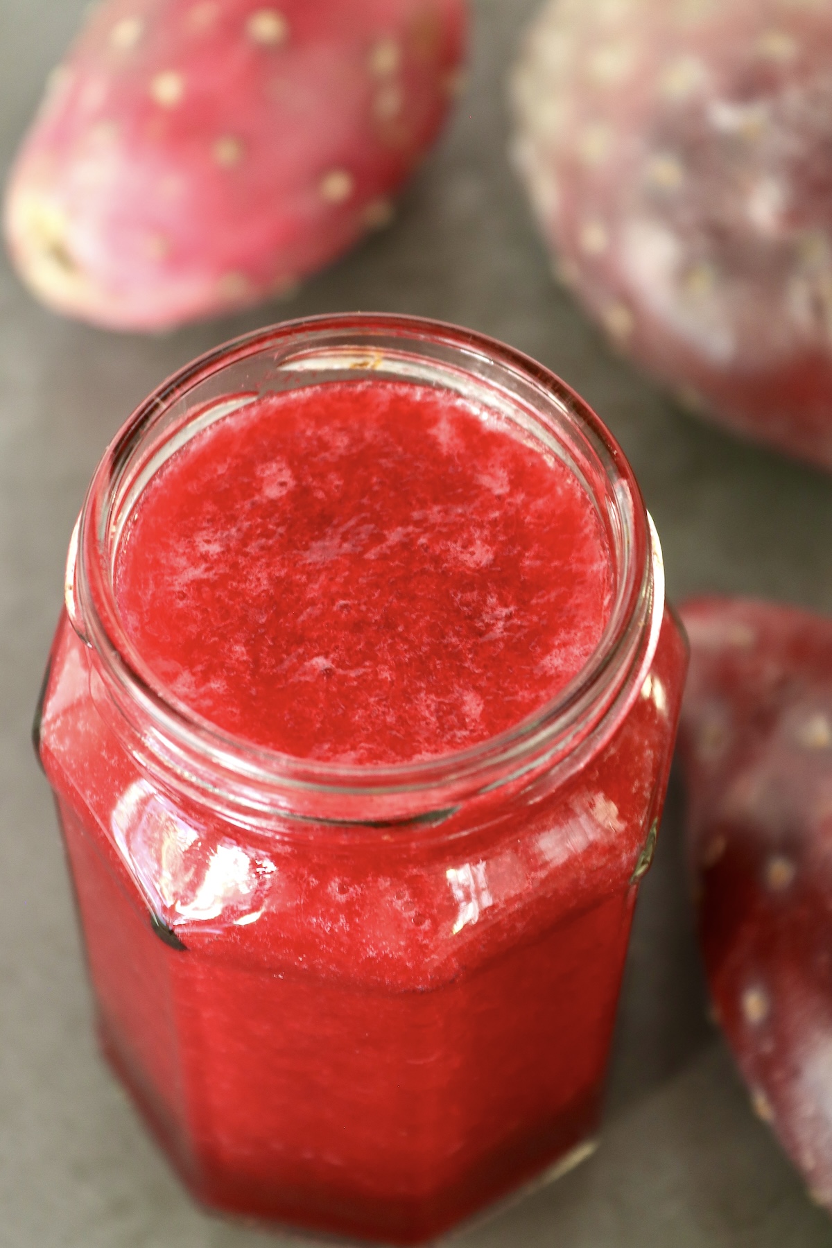 Top view of a full jar of prickly pear (cactus pear) juice with a few whole prickly pears next to it.