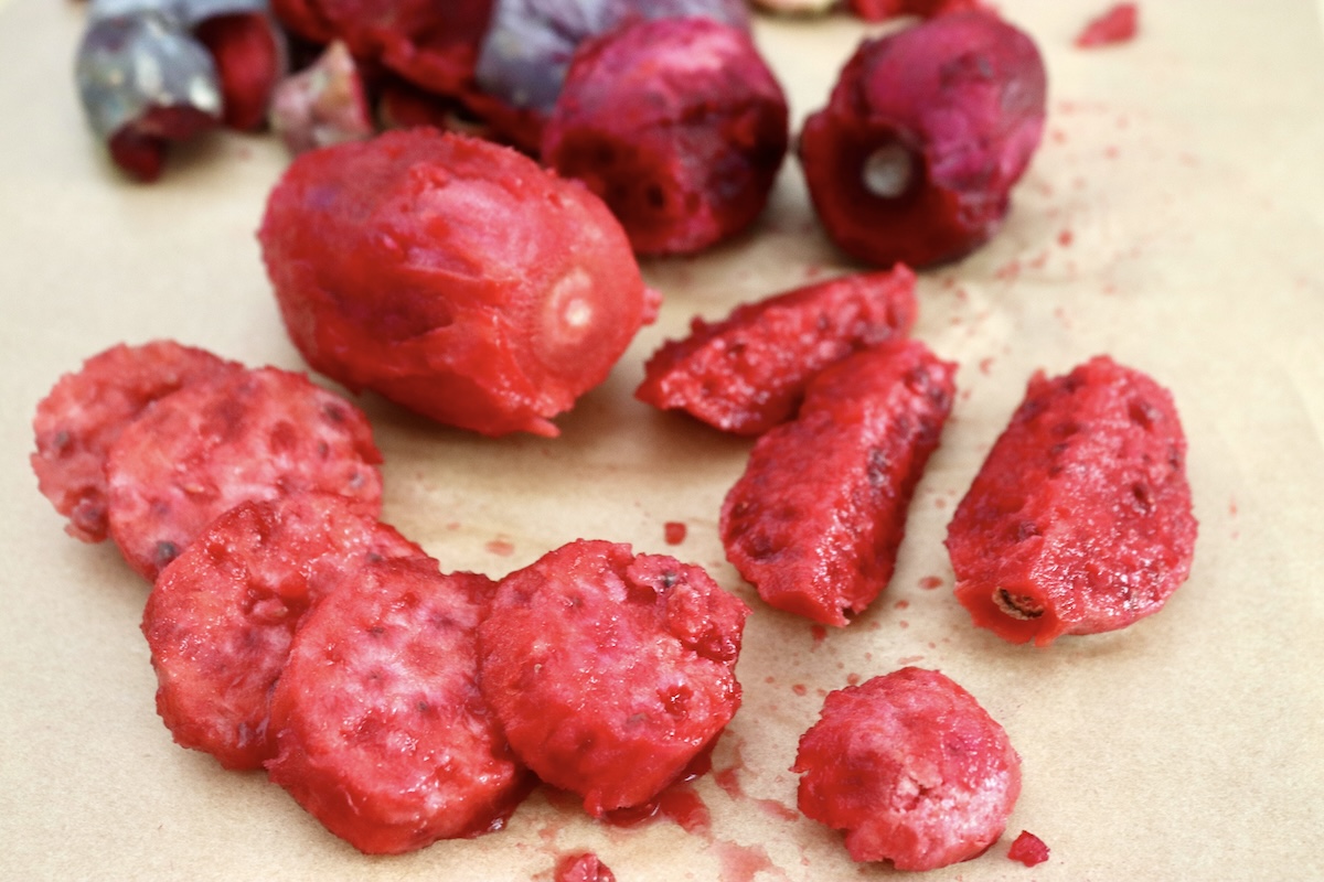 Several pieces of cut cactus pears (prickly pears) on cutting board with a few still left whole beind them.