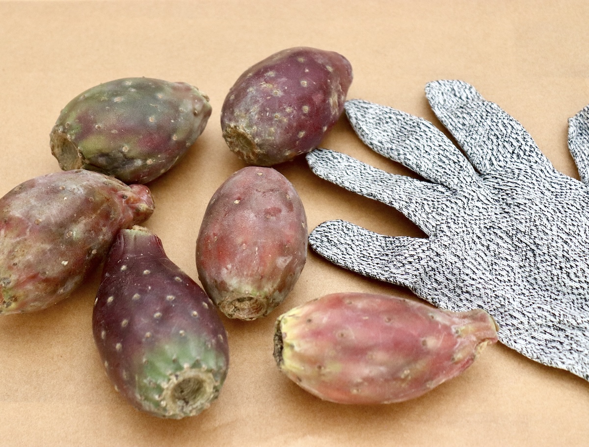 One cooking glove next to a few prickly (cactus) pears, on a cutting board.